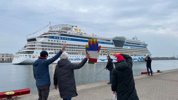 Menschen beobachten vom Ufer aus das Kreuzfahrtschiff AIDAdiva, das  in den Rostocker Hafen einfährt. © NDR Foto: Jürn-Jakob Gericke