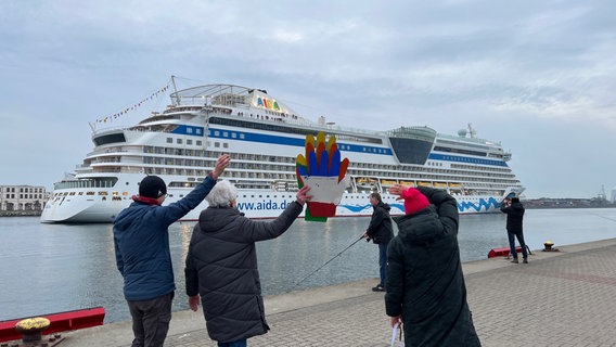 Menschen beobachten vom Ufer aus das Kreuzfahrtschiff AIDAdiva, das  in den Rostocker Hafen einfährt. © NDR Foto: Jürn-Jakob Gericke