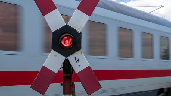 Ein Personenzug der Deutschen Bahn fährt hinter einem blinkenden Andreaskreuz an einem Bahnübergang in der Nähe von Schwerin vorbei. © Picture Alliance/dpa Foto: Jens Büttner
