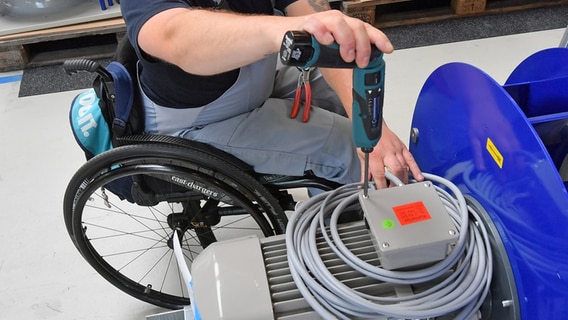 An einem Arbeitsplatz für Motorklemmen ist ein Mitarbeiter im Rollstuhl mit Montagearbeiten beschäftigt. © dpa Foto: Hendrik Schmidt/zb