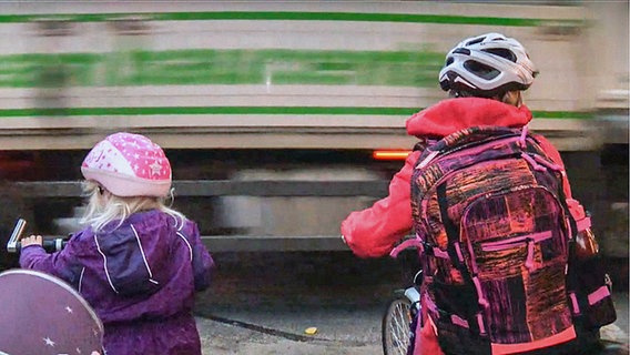 Zwei Kinder auf Fahrrädern warten an einer befahrenen Straße in Dettmannsdorf.  