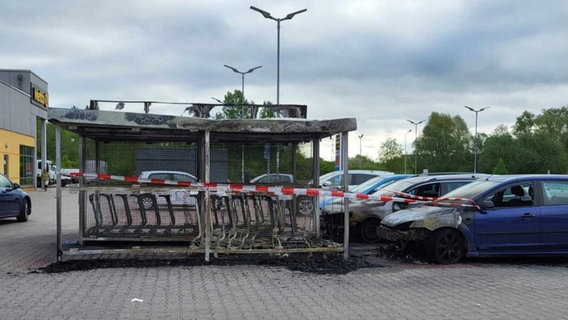 Zwei ausgebrannte Autos und ein ausgebrannter Unterstand für Einkaufswagen auf dem Parkplatz eines Supermarkts im Rostocker Stadtteil Toitenwinkel. © NonstopNews Rostock Foto: Stefan Tretropp