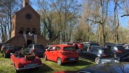 Besetzte Autos stehen vor einer Kirche, Pastor predigt vor dem Eingang der Kirche. Foto: Christopher Niemann