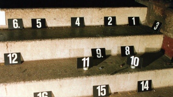 16 schwarze Tafeln mit weißen Nummern stehen 1993 auf den Stufen einer Treppe im Bahnhof von Bad Kleinen. Sie markieren Spuren, die die Polizei bei den Ermittlungen nach den Schüssen auf dem Gelände entdeckt hat. © NDR Foto: NDR