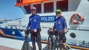 Uniformierte Polizisten im Bäderdienst stehen mit Fahrrädern vor einem Polizeischiff. © NDR Foto: Max Fuhrmann