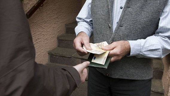 Ein Mann hält mehrere 50-Euro-Scheine in der Hand um sie einer anderen Person zu geben. © imago/imagebroker 