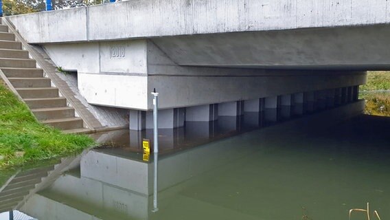 Der aufgestaute Stegenbach fließt unter einer Brücke hindurch. Vom Pegelstab ist nur noch die mit "100" beschriftete Spitze zu sehen. © Jens Uhthoff Foto: Jens Uhthoff