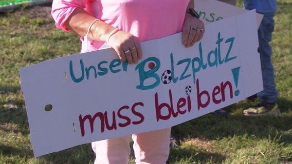 Eine Frau hält ein selbst gemaltes Schild mit der Aufschrift "Unser Bolzplatz muss bleiben!" in den Händen © NDR Foto: Screenshot