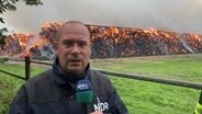 NDR MV Reporter Christoph Kümmritz steht vor einer brennenden Strohmiete. © NDR 