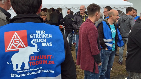 Streikende Mitarbeiter von Schmitz-Cargobull in Toddin. Neben dem Logo der IG Metall steht auf einer Jacke "Wir streiken euch was". © NDR Foto: Christoph Kümmritz