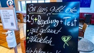 Vor einem Laden in einem Einkaufszentrum in Stralsund steht ein Schild mit dem Schriftzug "Bei uns gilt die 2G+Regelung+Test - gut gelaunt - glücklich"- © dpa-Bildfunk Foto: Stefan Sauer