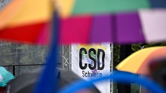 Regenbogenfarbene Regenschirme sind vor einem Schild mit der Aufschrift "Schwerin" zu sehen. © dpa Bildfunk Foto: Frank Hormann