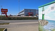 Blick auf das Norma-Logistikzentrum in Dummerstorf. Vorne rechts im Bild ist ein Trafohäuschen zu sehen, auf das ein Leuchtturm gemalt ist. © IMAGO / BildFunkMV Foto: IMAGO / BildFunkMV