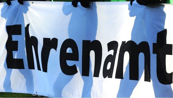 Ein Banner mit dem Aufdruck "Ehrenamt" wird von Personen hochgehalten. © dpa - Bildfunk Foto: Patrick Seeger