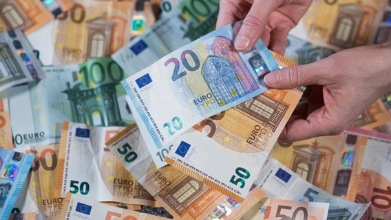 Zwei Hände halten zwei Geldscheine über einen ganzen Stapel von Banknoten. © dpa-Bildfunk Foto: Jens Büttner