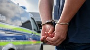 Ein Mann mit Handschellen steht vor einem Polizeiwagen. © picture alliance / Fotostand | Fotostand / K. Schmitt Foto: K. Schmitt