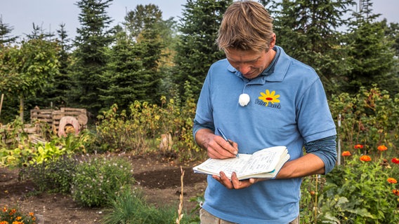 Ein Gärtner notiert etwas in ein Buch. © NDR Foto: Udo Tanske