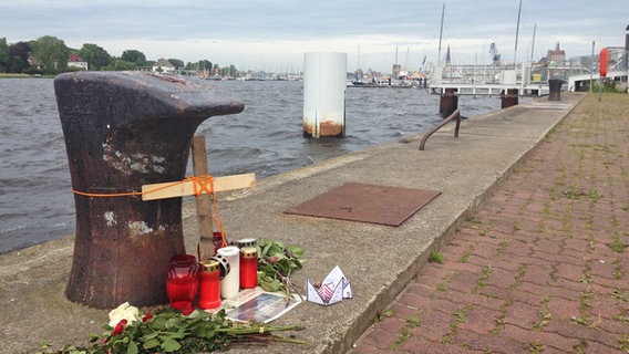 Kerzen und Rosen vor dem Poller, an dem die Georg Büchner im Rostocker Hafen befestigt war. © NDR Foto: Jan Heidebreck
