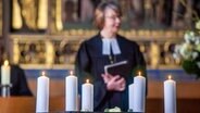 Schwerin: Die evangelische Landesbischöfin Kristina-Kühnbaum-Schmidt steht bei einem ökumenischen Gottesdienst zur Erinnerung an die Toten und Leidtragenden der Corona-Pandemie im Schweriner Dom hinter brennenden Kerzen. © dpa-Bildfunk Foto: Jens Büttner/dpa-Zentralbild