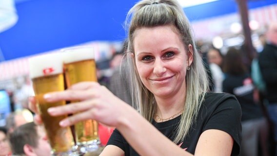 Eine Frau am Stand der Störtebeker Braumanufaktur hält lächelnd zwei blonde Bier in die Kamera. © Messe Berlin Foto: NDR