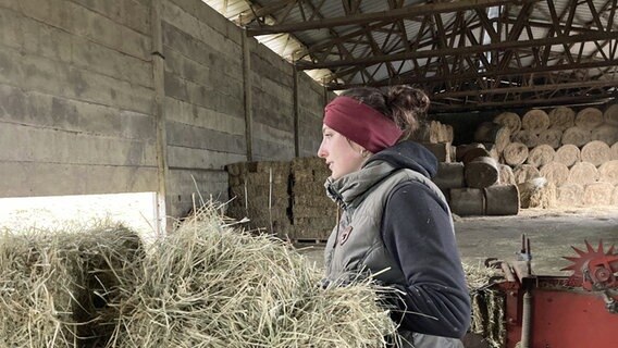 Charlotte Linder trägt einen Ballen Heu in einer großen Halle auf dem Gut Bisdorf © Svenja Winter / Charlotte Linder Foto: Svenja Winter / Charlotte Linder