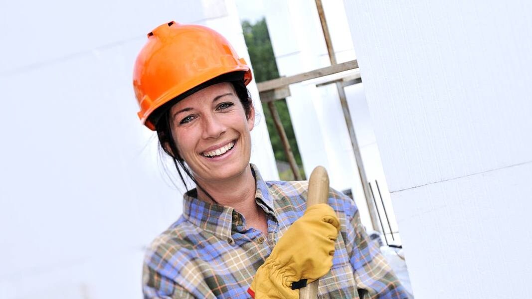 Symbolbild: Frau mit Helm und in Arbeitskleidung.