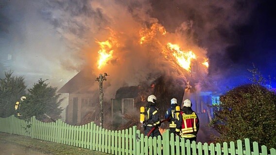 Ein Reeddachhaus steht in Flammen. Einsatzkräfte der Feuerwehr löschen.  Foto: TILO WALLRODT