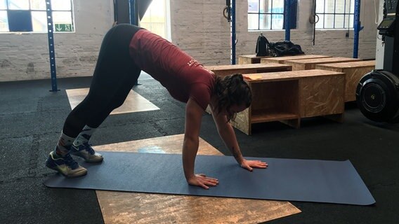 Trainerin bewegt sich in einer Art Krebsgang über eine Yogamatte. Trainerin bewegt sich in einer Art Krebsgang über eine Yogamatte. © NDR Foto: Golo Schmiedt