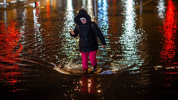 Eine Frau geht durch das Hochwasser am Stadthafen in Wismar. Wegen einer erwarteten Sturmflut an der Ostseeküste sind Uferbereiche in der Nähe des Hafens teilweise überflutet. © dpa Foto: Jens Büttner