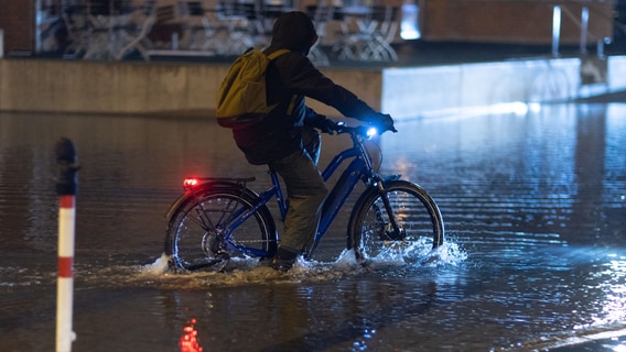 Ein Radfahrer fährt am Morgen durch das Hochwasser am Stadthafen in Wismar. © dpa Foto: Jens Büttner