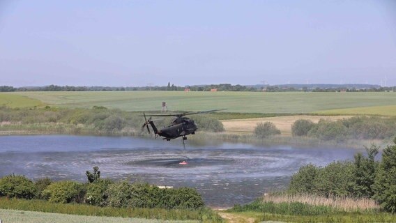 Ein Hubschrauber der Bundeswehr entnimmt Wasser aus einem See nahe des in Brand geratenen Gördenitzer Moors. © NonstopNews Rostock Foto: Stefan Tretropp