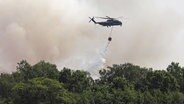 Ein Hubschrauber der Bundeswehr kippt Wasser aus einem angehängten Behälter auf Brandherde im Göldenitzer Moor. © NonstopNews Rostock Foto: Stefan tretropp