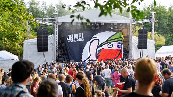 Der Schriftzug "Jamel rockt den Förster" hängt bei einer Umbaupause vor der Bühne. Davor stehen Hunderte Zuschauer. © dpa Foto: Rainer Jensen