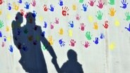 Der Schatten von Vater und Kind fällt auf eine bunt mit Händen bedruckte Wand © dpa-Bildfunk Foto: Peter Kneffel/dpa