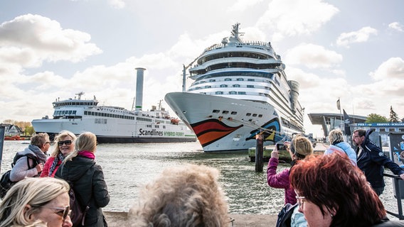 Gäste spazieren auf einer Port Party am Kreuzfahrthafen in Warnemünde. Die AIDAmar eröffnet am Sonntag die diesjährige Kreuzfahrtsaison in Warnemünde und feiert den Start in die Kreuzfahrtsaison 2024 mit einer Port Party. © Frank Hormann/dpa Foto: Frank Hormann/dpa