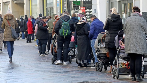 Eine lange Schlange mit wartenden Menschen steht in einer Einkaufsstraße in Rostock vor einem Geschäft. © dpa-Bildfunk Foto: Bernd Wüstneck