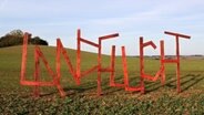 Auf einem Feld steht in großen Holzbuchstaben das Wort "Landflucht". © Kunst-Kolchose, Neu Karin 