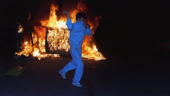 Junger Mann vor einem Feuer bei schweren Krawallen im August 1992 in Rostock-Lichtenhagen. © picture-alliance / ZB - Fotoreport Foto: Jan Bauer