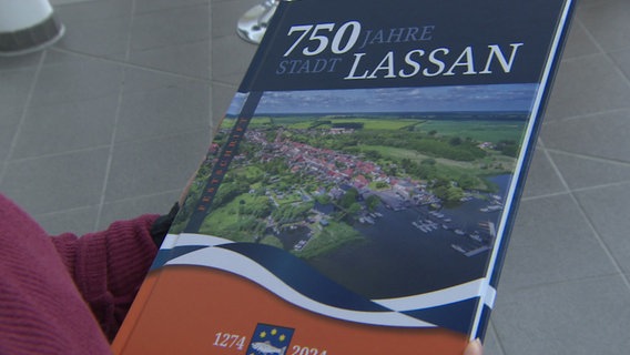 Das Buch "750 Jahre Stadt Lassan" wird in die Kamera gehalten. © NDR Foto: Screenshot