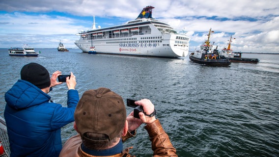 Das zuletzt als Wohnschiff für auswärtige Werftarbeiter genutzte Kreuzfahrtschiff "Superstar Libra" wird von mehreren Schleppern vom Werfthafen Wismar in die Ostsee gezogen. © dpa-Bildfunk Foto: Jens Büttner