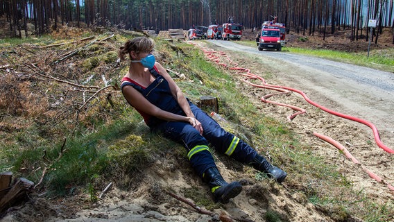 Eine erschöpfte Feuerwehrfrau sitzt in der Nähe der evakuierten Ortschaft Alt Jabel an einem Versorgungsweg. © dpa Zentralbild Foto: Jens Büttner