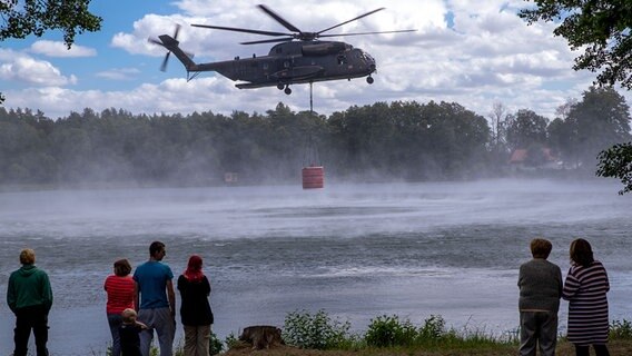 Unter den Augen Schaulustiger nehmen Hubschrauber Löschwasser in einem See auf. © Jens Büttner/dpa-Zentralbild/ Foto: Jens Büttner/dpa-Zentralbild/