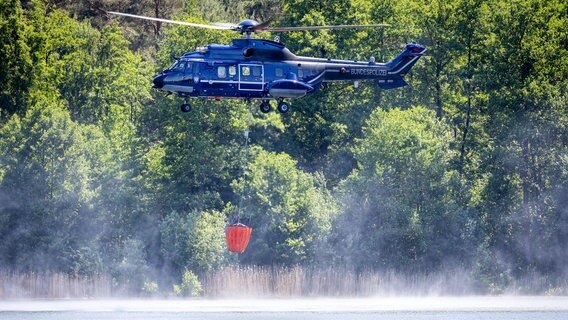 Ein Hubschrauber der Bundespolizei nimmt aus einem See Löschwasser zur Bekämpfung eines Waldbrands auf einem ehemaligen mit Munition verseuchten Truppenübungsplatz auf. © dpa Foto: Jens Büttner