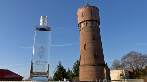 Eine eckige Wasserflasche mit der Aufschrift "Minus 181". Im Hintergrund ist der Wasserturm von Parchim zu sehen. © NDR Foto: NDR