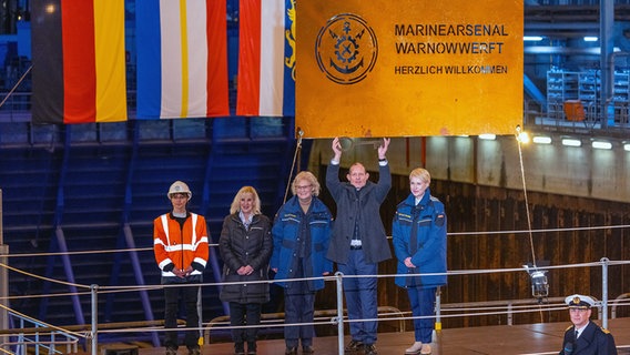 Rostock: Christine Lambrecht (SPD, M), Bundesministerin der Verteidigung, Manuela Schwesig (SPD, r), die Ministerpräsidentin von Mecklenburg-Vorpommern, Rainer Sacher, Direktor des Marinearsenals, Gabriele Korb 2.v.l.), Präsidentin vom Bundesamt für Ausrüstung, Informationstechnik und Nutzung der Bundeswehr (BAAINBw) sowie Manja Zeidler, Sicherheitsbeauftragte des Werftstandorts, stehen nach der offiziellen Inbetriebnahme des neuen Marinearsenals Warnowwerft vor dem Trockendock. © Jens Büttner/dpa +++ dpa-Bildfunk +++ Foto: Jens Büttner/dpa +++ dpa-Bildfunk +++