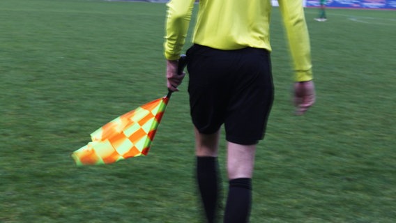 Ein Schiedsrichter geht mit einer Abseitsflagge auf einem Fußballfeld. Ein Schiedsrichter geht mit einer Abseitsflagge auf einem Fußballfeld. © NDR Foto: Wiebke Heiden