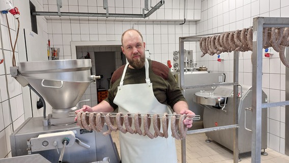 Wild-Fleisch-Experte Martin Brodoch steht in seinem Produktionsraum und hält eine Stange mit frischen Wild-Würsten in der Hand. © NDR/Stefan Thoms Foto: Stefan Thoms