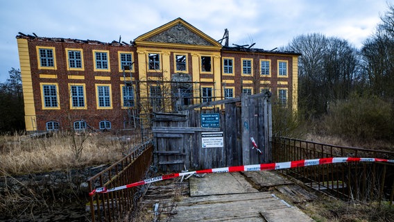 Ein Absperrband der Polizei hängt an der einzigen Brücke zum abgebrannten Wasserschloss Johannstorf. © Jens Büttner 