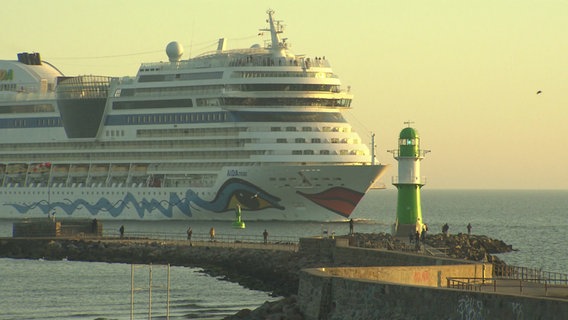 Das Schiff AIDAmar fährt in der aufgehenden Morgensonne am grünen Molenfeuer in Warnemünde ein. © NDR Foto: Screenshot NDR