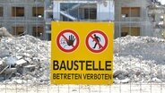 Großes, gelbes Schild mit der Aufschrift: "Baustelle betreten verboten" sowie mit Warnpiktogrammen, befestigt mit Kabelbindern an einem Bauzaun einer Baustelle. © Torsten Sukrow 